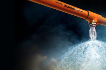 An orange pipe emits a thick plume of white smoke or steam against a dark sky.